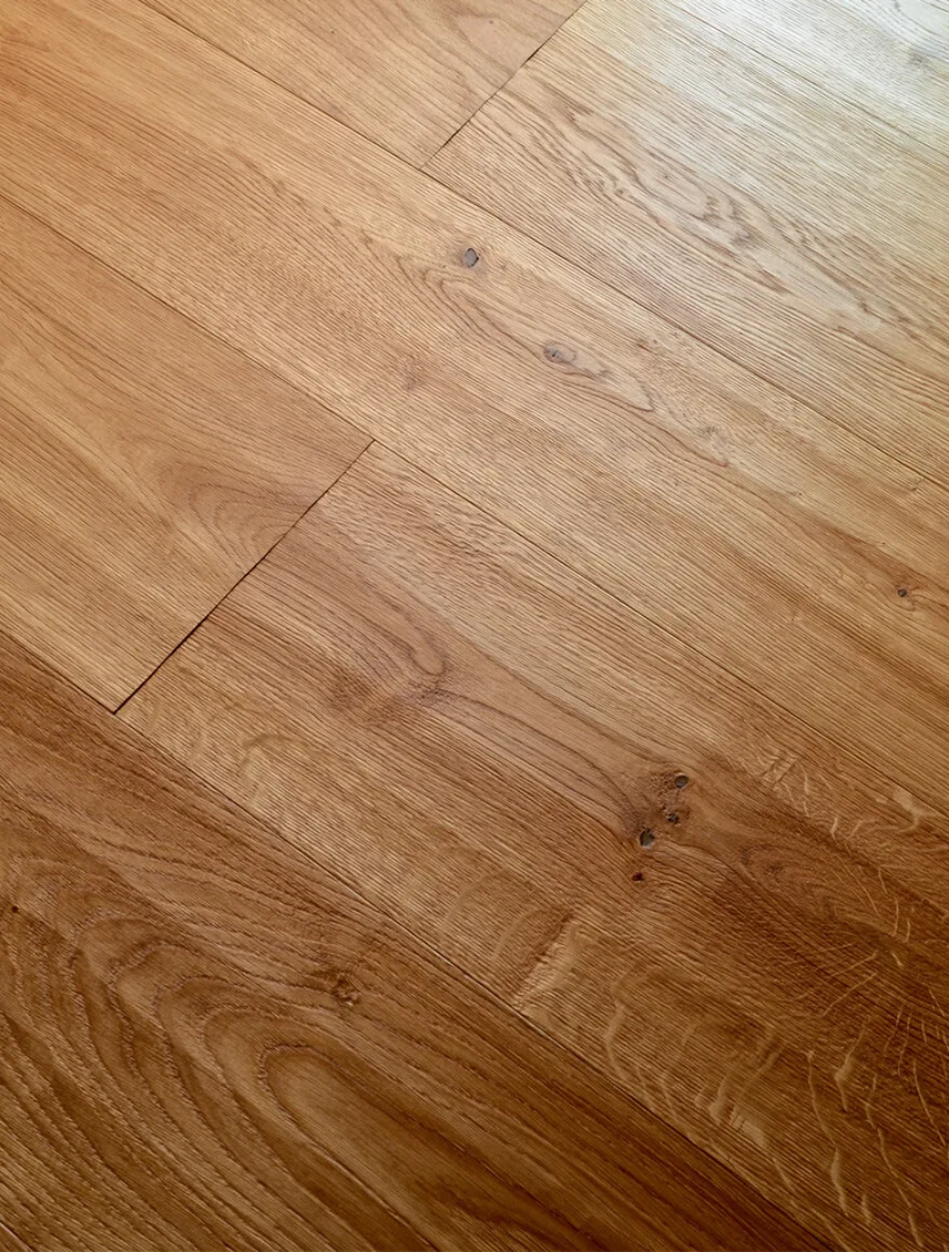 Detailní šikmý pohled na strukturu dubové podlahy v teplém odstínu kolekce Honey, kde jsou jasně patrné suky, letokruhy a přirozené barevné variace dřeva.