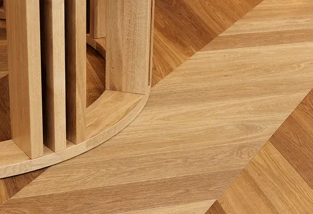 Detailní záběr na texturu světlé dřevěné podlahy v šedavém odstínu s výraznou kresbou letokruhů a plynulým přechodem stínu, který podtrhuje přirozený povrch materiálu.