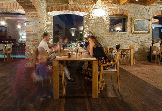 Rustikální interiér restaurace s kamenným zdivem, klenbami a tmavou dubovou podlahou v dekoru Hazel, doplněný masivním dřevěným nábytkem.