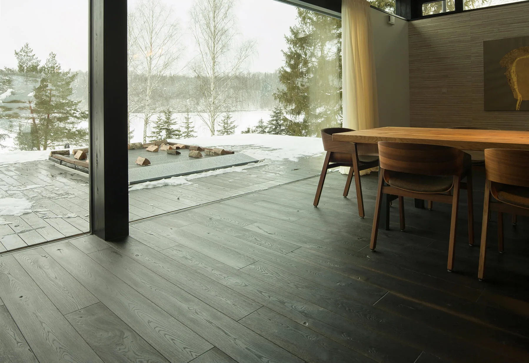 Moderní interiér vily Trnávka s tmavou dubovou podlahou z kolekce Ink, prosklenou stěnou s výhledem na zasněženou krajinu a jídelním stolem z masivního dřeva.