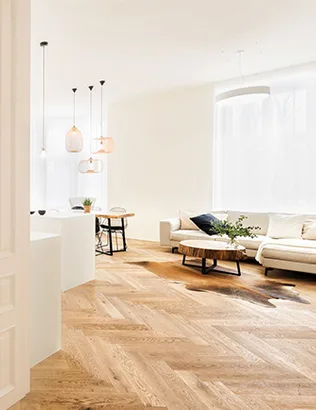 Světlý moderní obývací pokoj v historickém objektu s dubovou podlahou Oakcent v klasickém stromečkovém vzoru, bílou pohovkou a designovým stolkem z masivního dřeva.