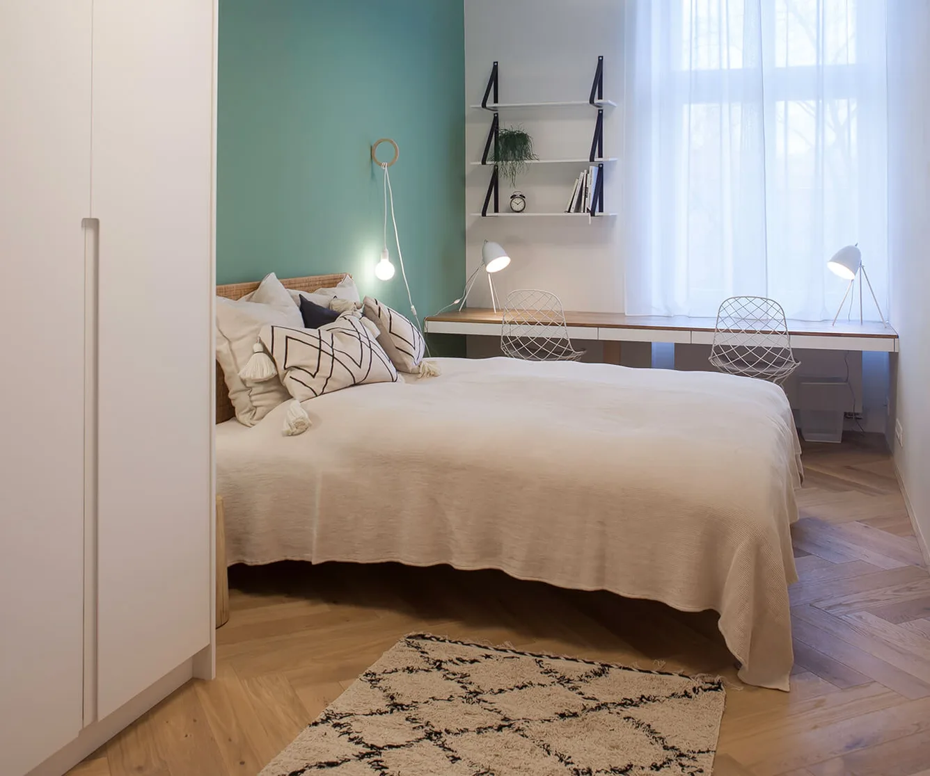 Moderní ložnice v historickém bytě s dubovou podlahou Oakcent (herringbone), tyrkysovou stěnou a minimalistickým pracovním koutem.