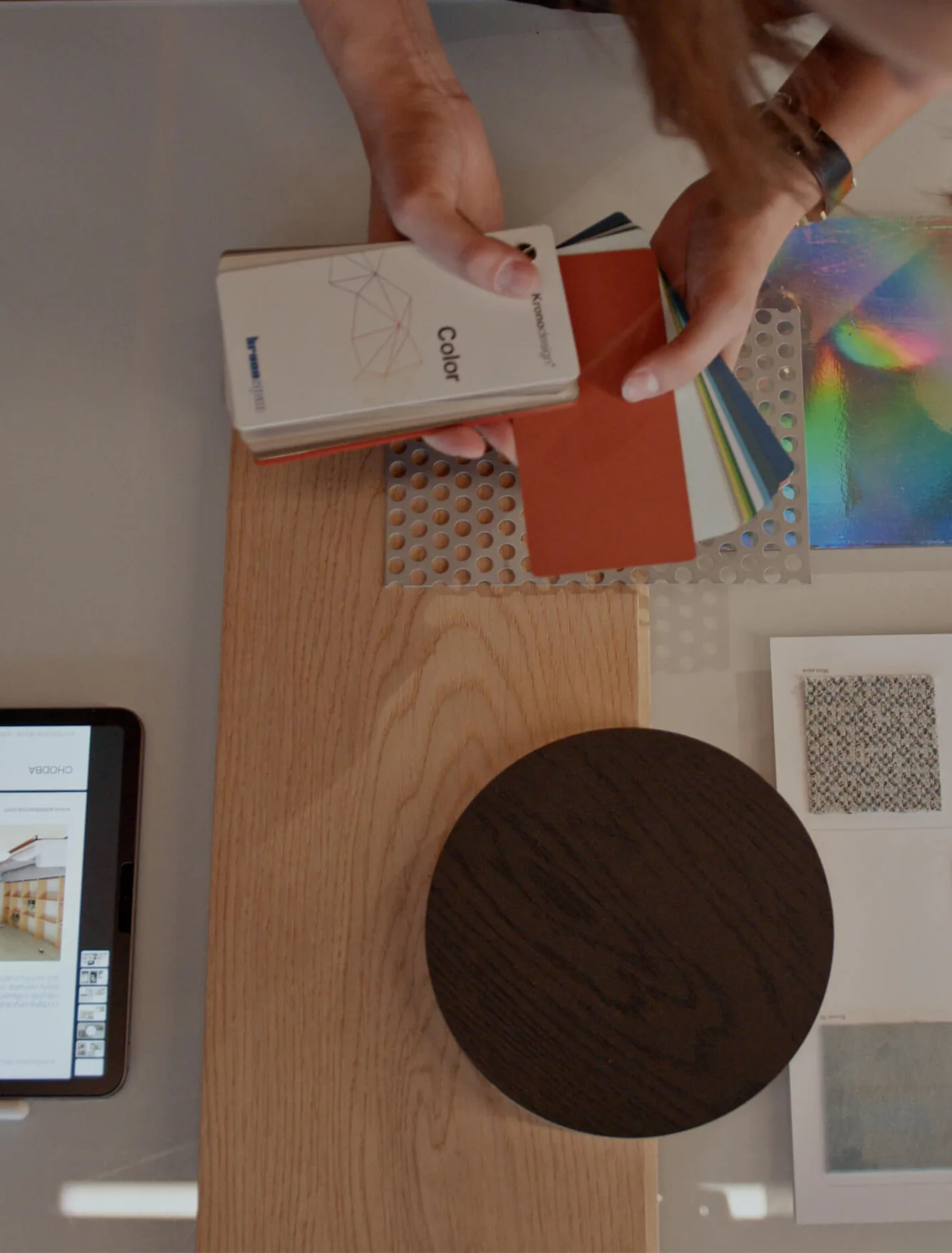 Detailní pohled na proces navrhování interiéru, kde designérka vybírá barevné vzorníky a materiály na vzorku světlé dubové podlahy, doplněné o vzorek tmavého dřeva a textilií.