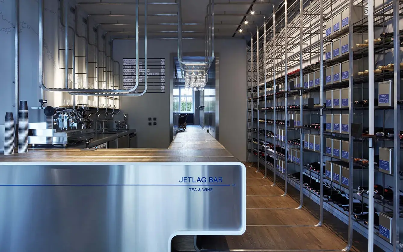 Moderní industriální interiér Jetlag Baru s nerezovým barem a policovým systémem na víno, kterému dodává hřejivou atmosféru přírodní dubová podlaha Oakcent v tmavším odstínu.