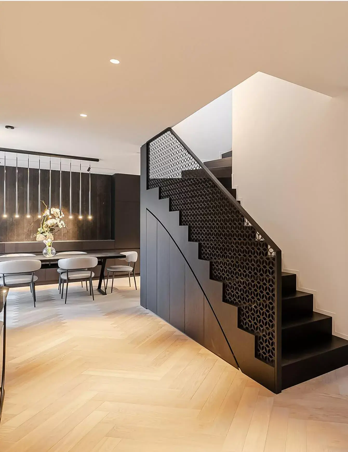 Moderní interiér jídelny v soukromém bytě na Josefově se světlou dubovou podlahou položenou do klasického stromečku, kterou doplňuje designové černé schodiště s dekorativním zábradlím a minimalistické osvětlení nad jídelním stolem.