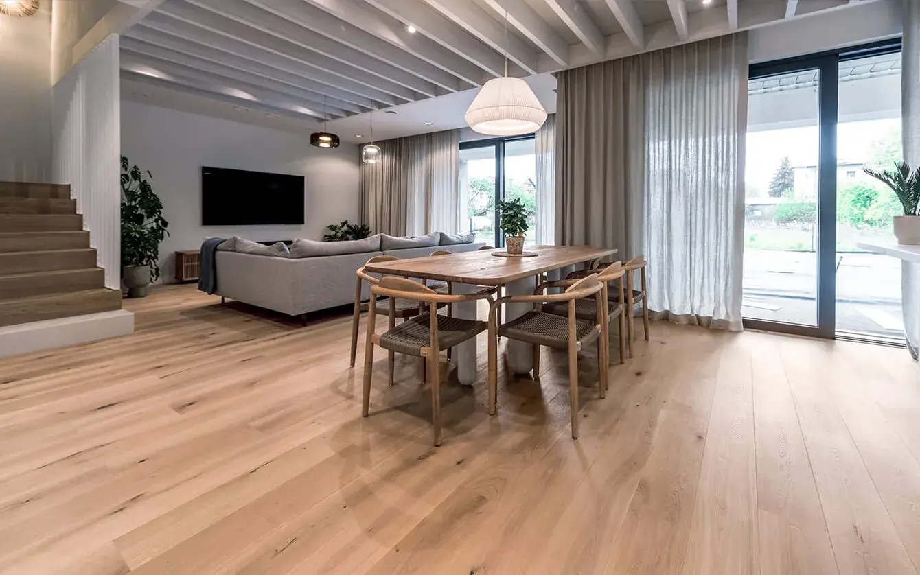 Moderní prosvětlený interiér obývacího pokoje s jídelnou v Soukromém domě Motyla, kterému dominuje přírodní dubová podlaha Oakcent a výrazný lamelový strop, doplněný o minimalistický nábytek v neutrálních tónech a velkoformátové prosklení do zahrady.