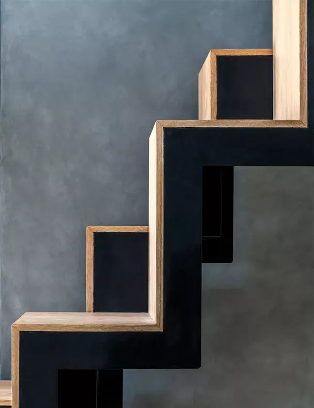 Detail nášlapů schodiště v kombinaci přírodního dubu a antracitových bočnic na pozadí šedé stěrky.