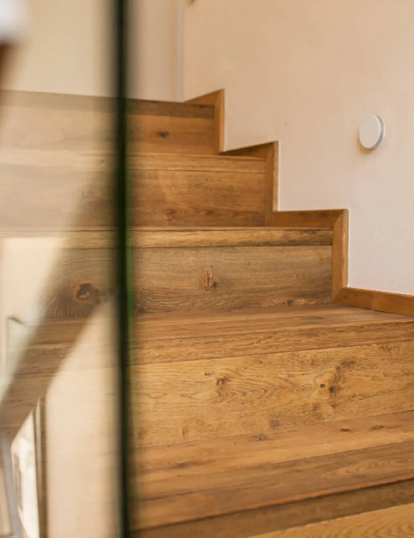 Detailní záběr na precizně zpracované dřevěné schodiště v soukromém domě v Uherském Hradišti, kde masivní dubové stupně s výraznou přírodní texturou a suky doplňuje minimalistické skleněné zábradlí.