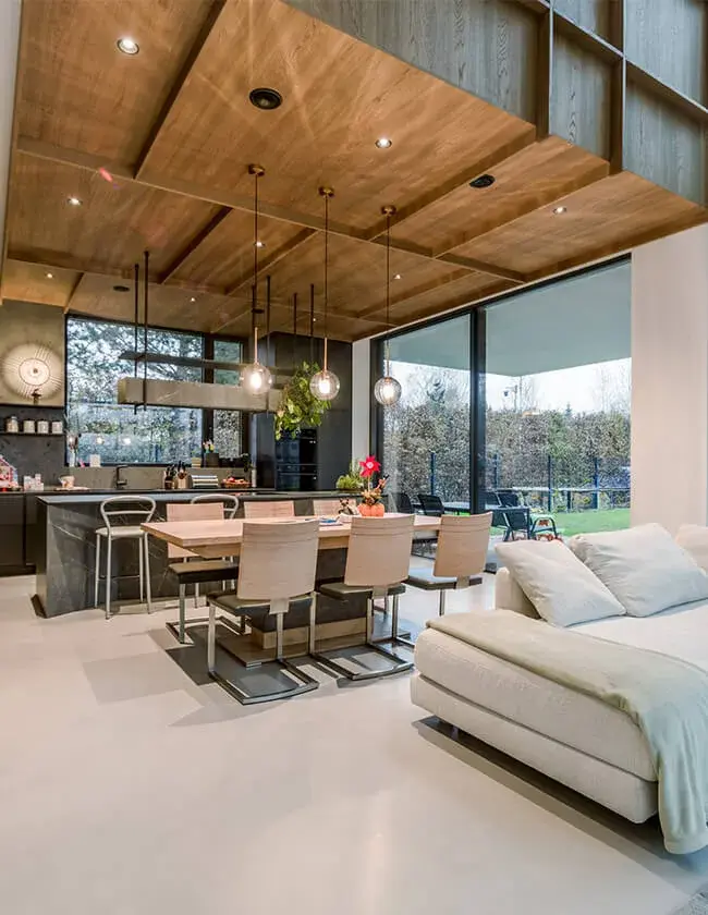 Moderní otevřený interiér Soukromé rezidence u Vratislavi s litou světlou podlahou, kterému dominuje výrazný dřevěný kazetový podhled s integrovaným osvětlením a jídelní kout s velkorysým prosklením do zahrady.