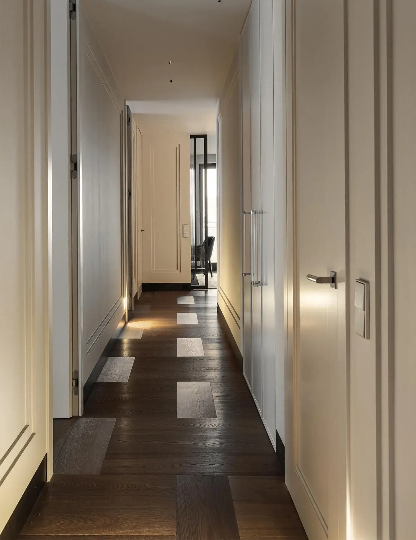 Interiér moderní chodby v projektu Stodola v Miloslavi, kde tmavá dubová podlaha z kolekce Hazel tvoří základ pro hravý design s nepravidelně vloženými světlými lamelami, které vedou pohled směrem k proskleným dveřím.