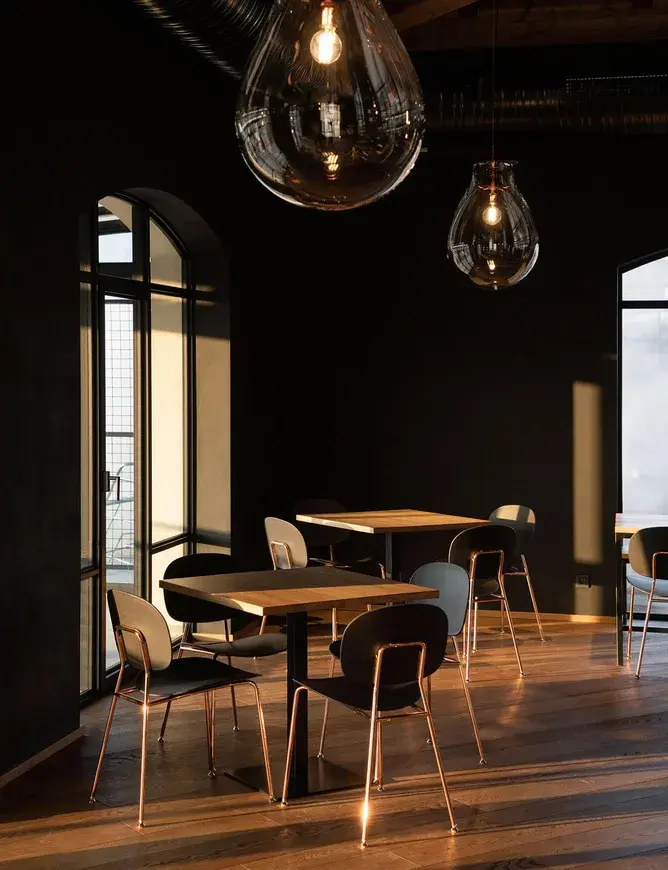 Industriální interiér Návštěvnického centra Bernard v Humpolci s tmavými stěnami a velkými klenutými okny, kde dubová podlaha z kolekce Sand v hřejivém přírodním odstínu prosvětluje prostor a tvoří základ pro moderní tmavý nábytek s měděnými detaily.