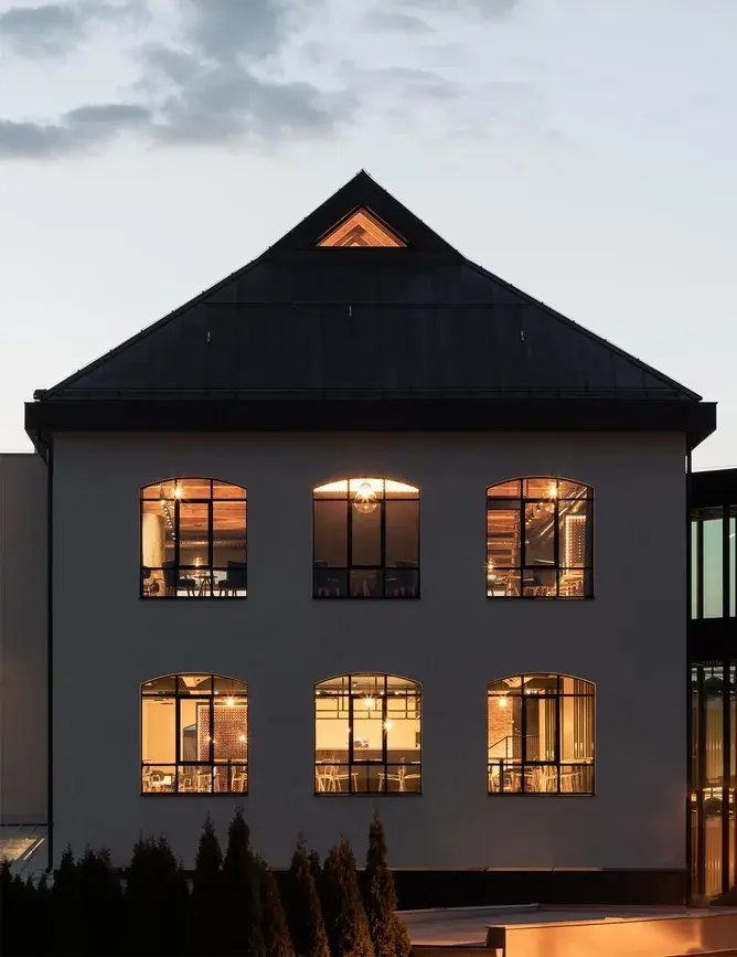 Večerní pohled na osvětlenou fasádu Bernard Visitor Center v Humpolci, kde skrze industriální okna vyniká hřejivý interiér s podlahami Oakcent.