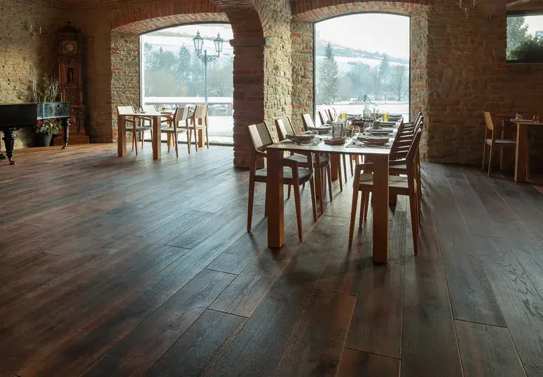 Široká tmavá dubová prkna Oakcent v historickém interiéru s kamennými zdmi, klenbami a výhledem skrze velkoformátová okna do zimní zahrady.