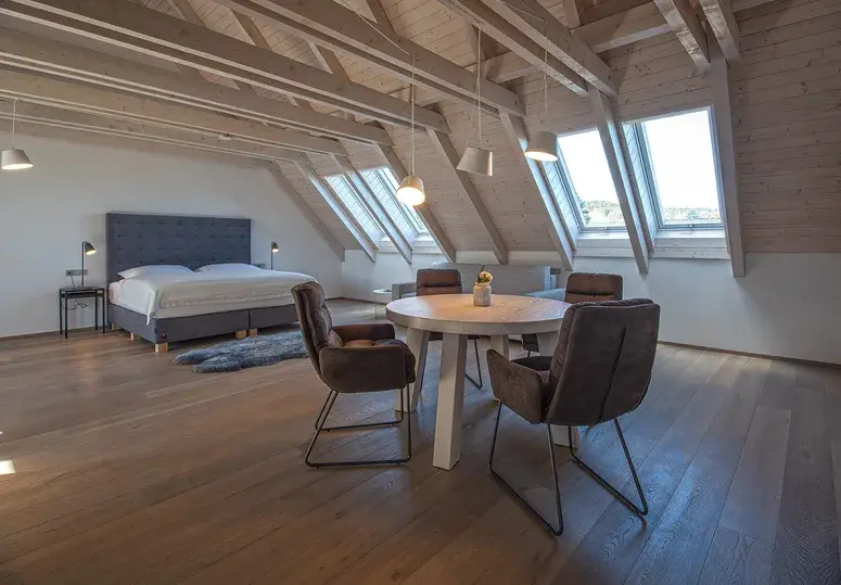 Prostorná podkrovní ložnice s přiznanými trámy a masivní dubovou podlahou Oakcent v přírodním hnědém odstínu.