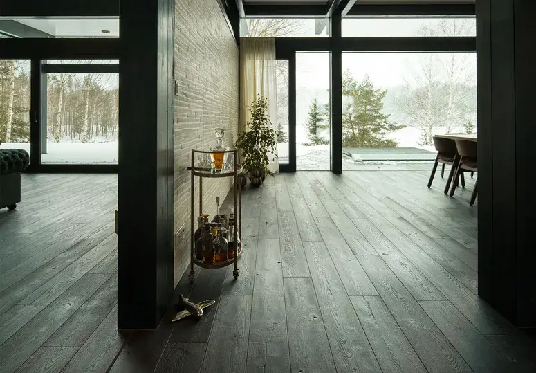 Luxusní tmavá dubová podlaha Oakcent s výraznou texturou v prostorném interiéru s prosklenými stěnami a výhledem do zimní krajiny.