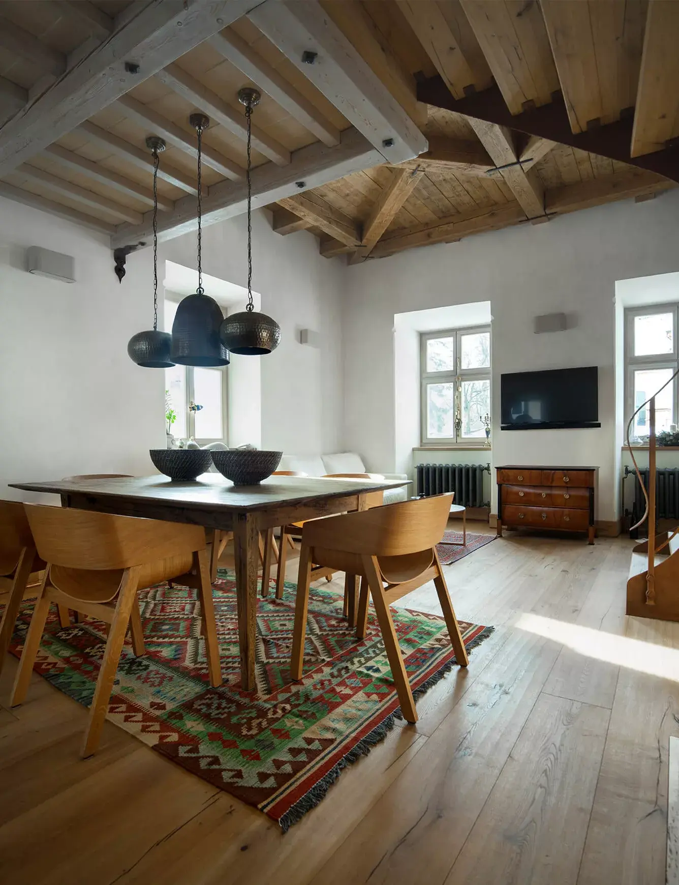 Rustikální interiér jídelny v historickém objektu Kaštiel Kubínyi s přiznanými dřevěnými trámy na stropě a ručně hoblovanou dubovou podlahou Oakcent Rustic, kterou doplňuje orientální koberec a dřevěný nábytek.