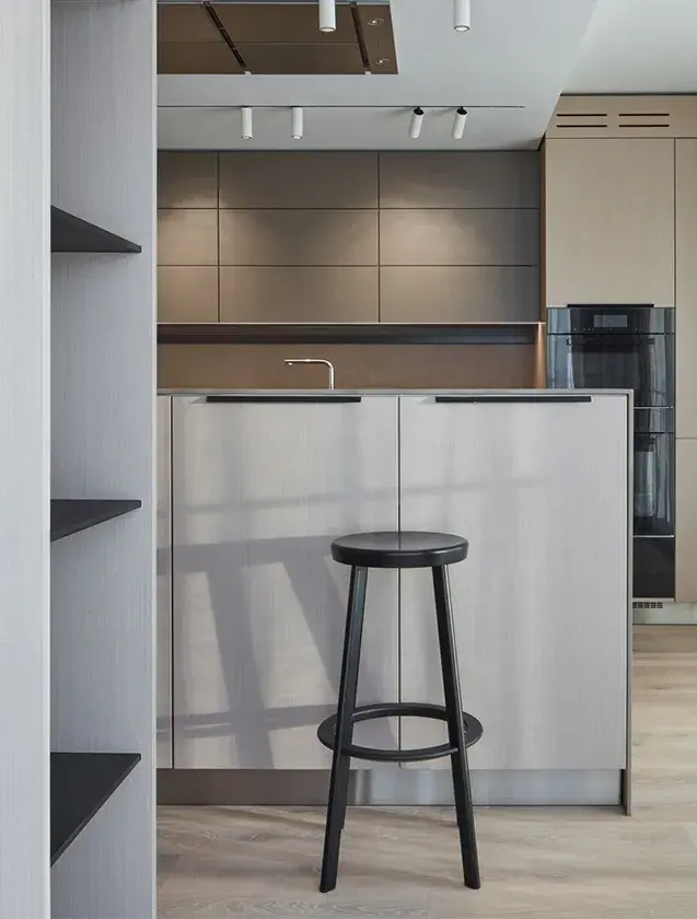 Moderní kuchyňský kout s nerezovým ostrůvkem a černou barovou židlí v bytě na Žižkově, kde světlá dubová podlaha Oakcent Rustic v Bianco oleji doplňuje minimalistický šedý design nábytku.