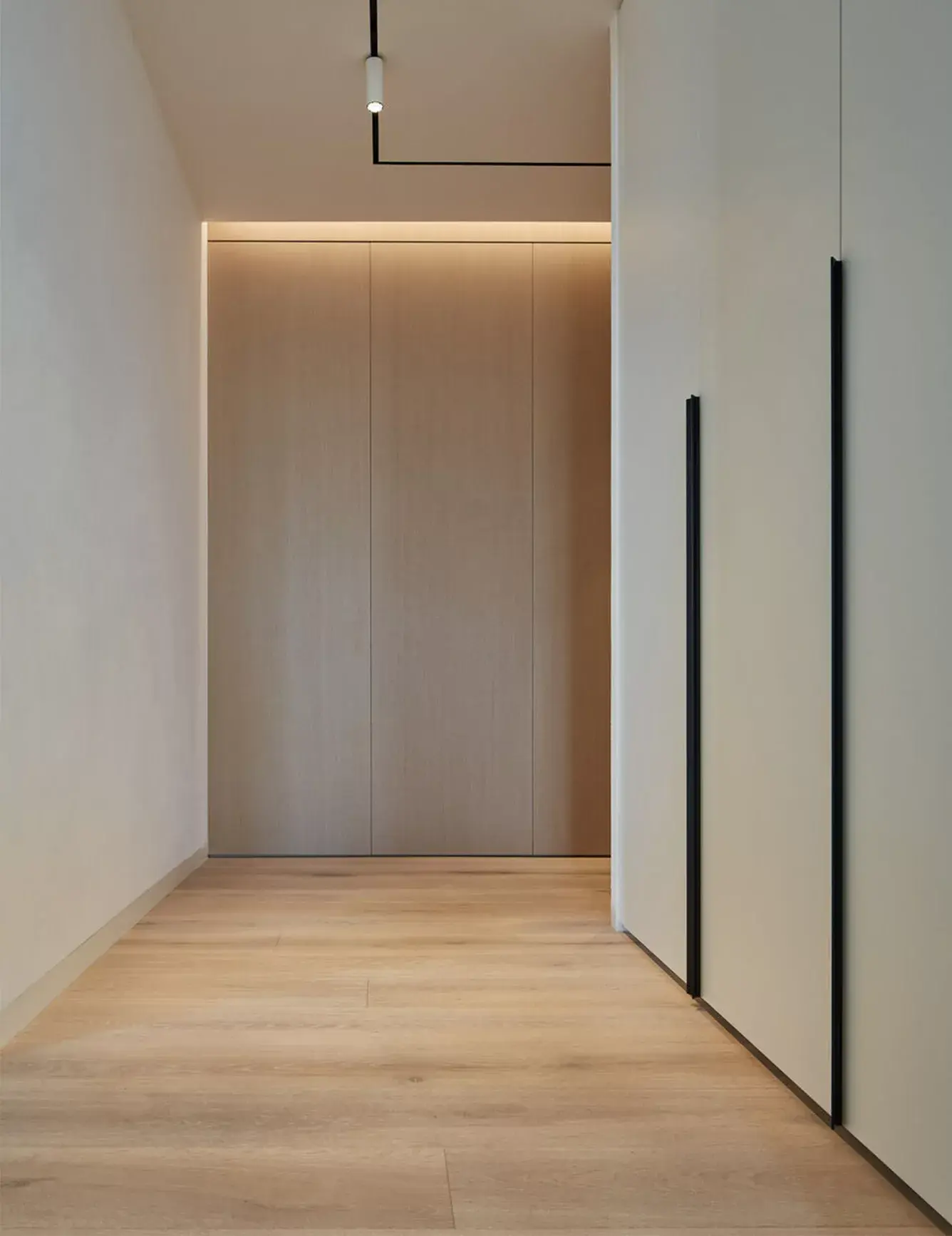 Celkový pohled na světlou chodbu v moderním pražském bytě s vestavnými skříněmi s černými úchyty, které doplňuje kartáčovaná dubová podlaha Oakcent Rustic v Bianco oleji.