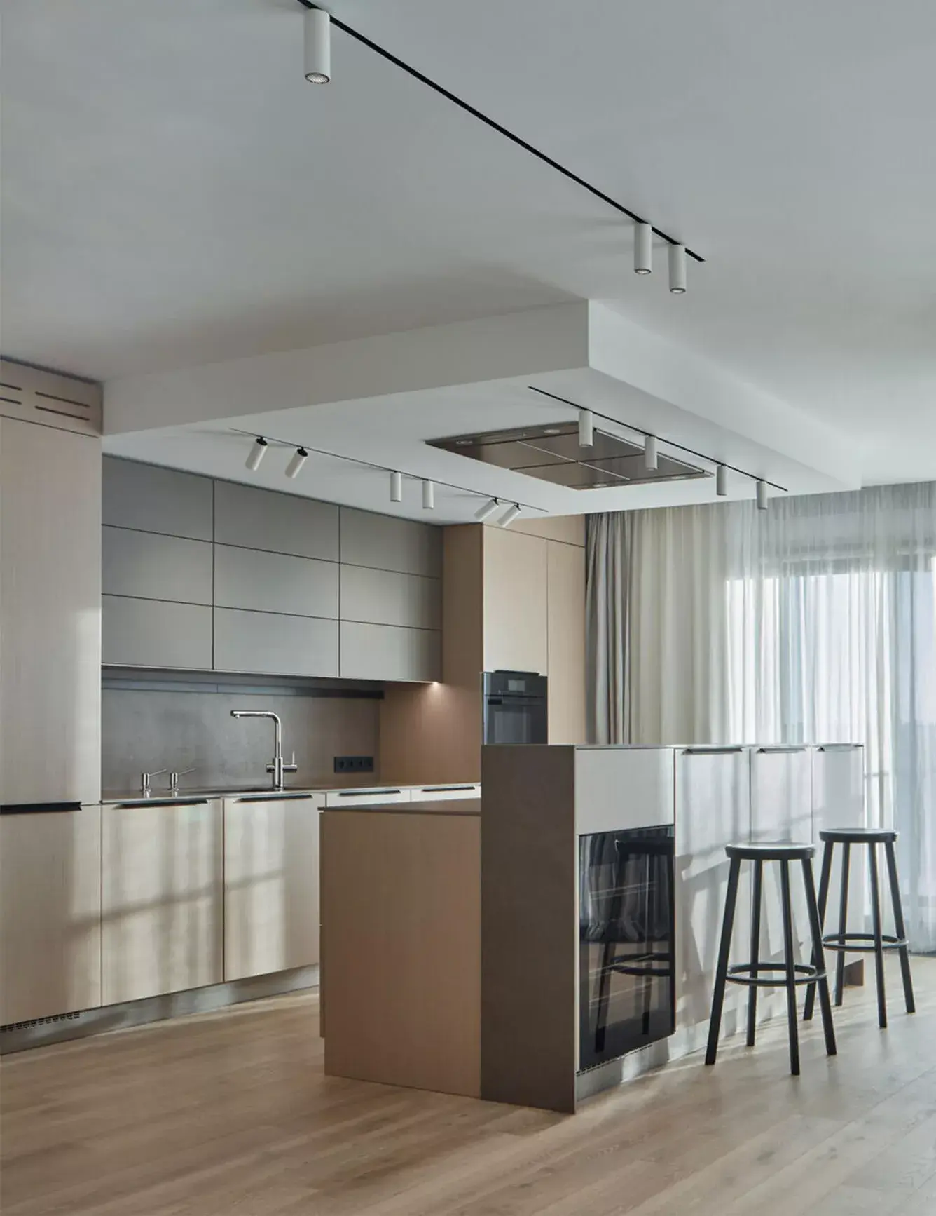 Celkový pohled na moderní kuchyni s ostrůvkem v pražském bytě, kde dubová podlaha Oakcent Rustic v odstínu Bianco doplňuje minimalistický šedý nábytek a technické osvětlení.