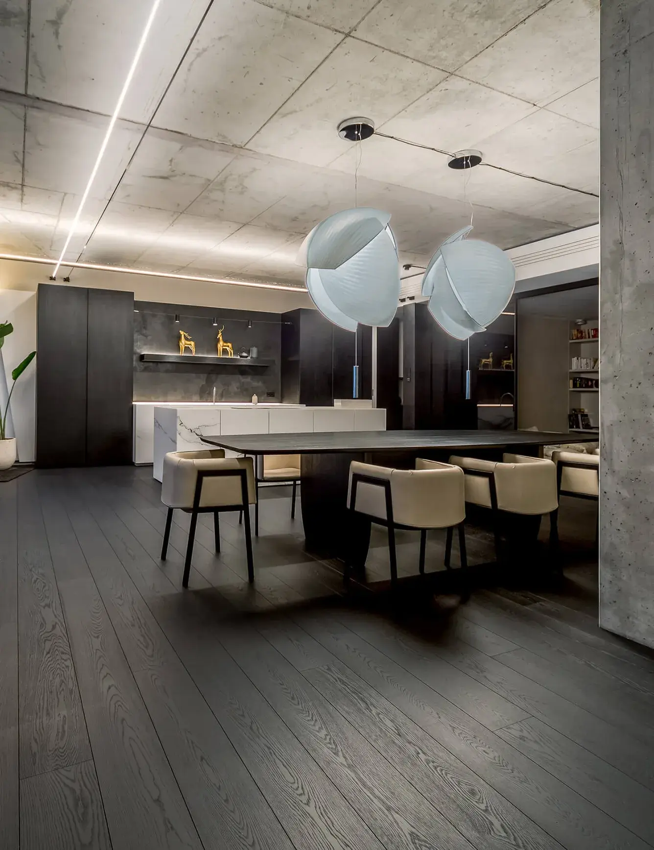 Luxusní interiér bytu Złota 44 s otevřeným prostorem jídelny a kuchyně, kde tmavá dubová prkna Oakcent Premium v odstínu Super Graphite harmonicky ladí s přiznaným betonovým stropem a minimalistickým bílým ostrůvkem.