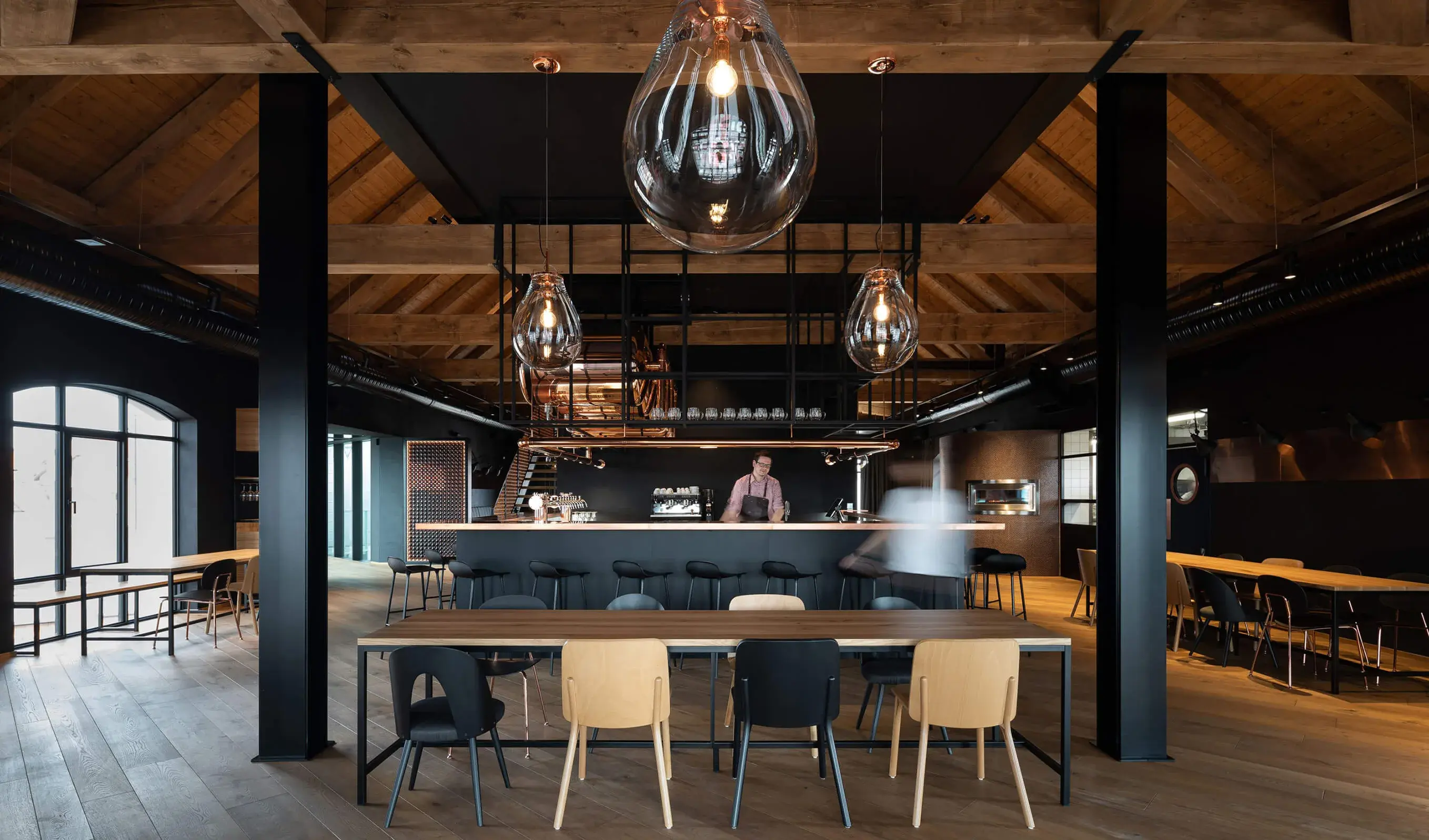 nteriér restaurace Bernard Visitor Center s tmavou dubovou podlahou Oakcent, černými stěnami a designovými skleněnými svítidly ve tvaru pivních kapek nad dřevěnými stoly.