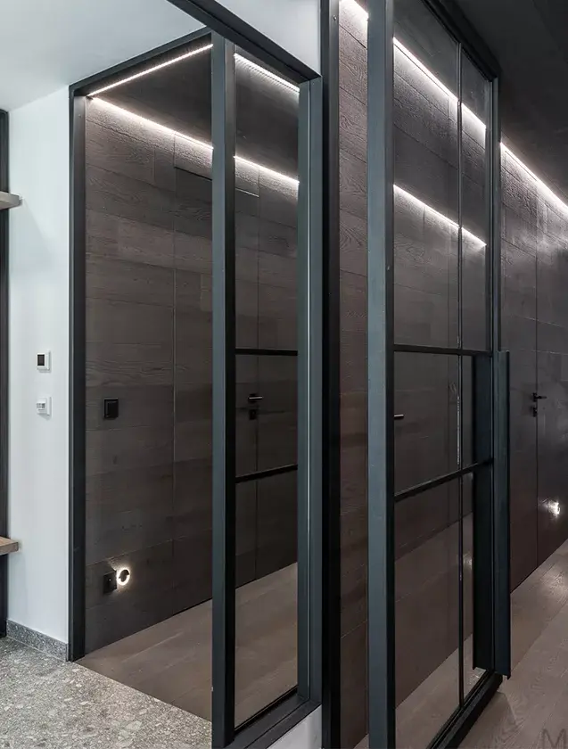 Moderní chodba s tmavě šedým dubovým obkladem stěn a podlahou Oakcent vedoucí k otevřenému ocelovému schodišti s výhledem do přírody v realizaci Apartmán Lipno.