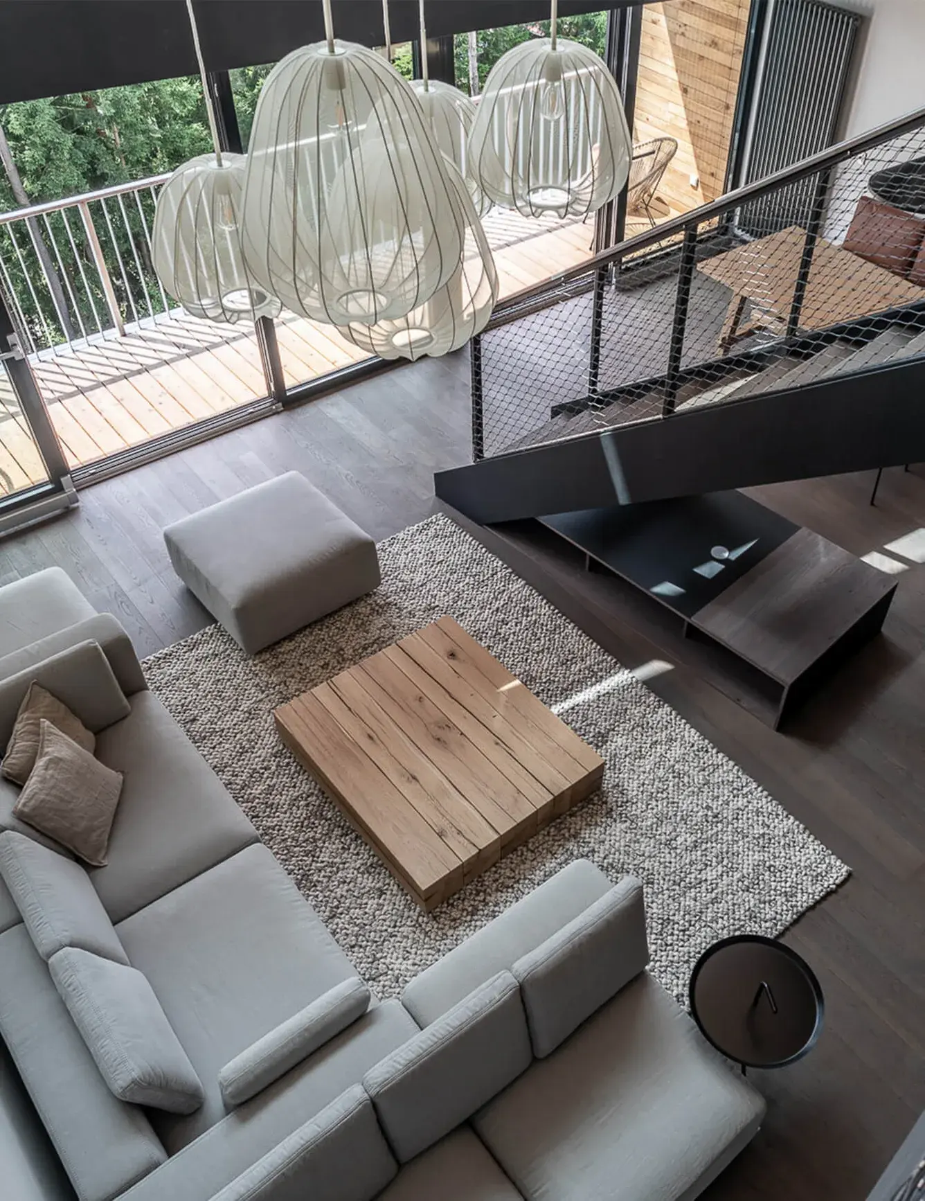 Pohled z výšky na moderní obývací pokoj v apartmánu Lipno s tmavou dubovou podlahou Oakcent, světlou rohovou sedací soupravou a konferenčním stolkem z masivního dubu, prosvětlený velkými okny vedoucími na terasu.