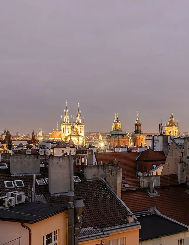 Panoramatický noční výhled ze soukromého apartmánu na Josefově na osvětlené historické věže Týnského chrámu a střechy pražského Starého Města.
