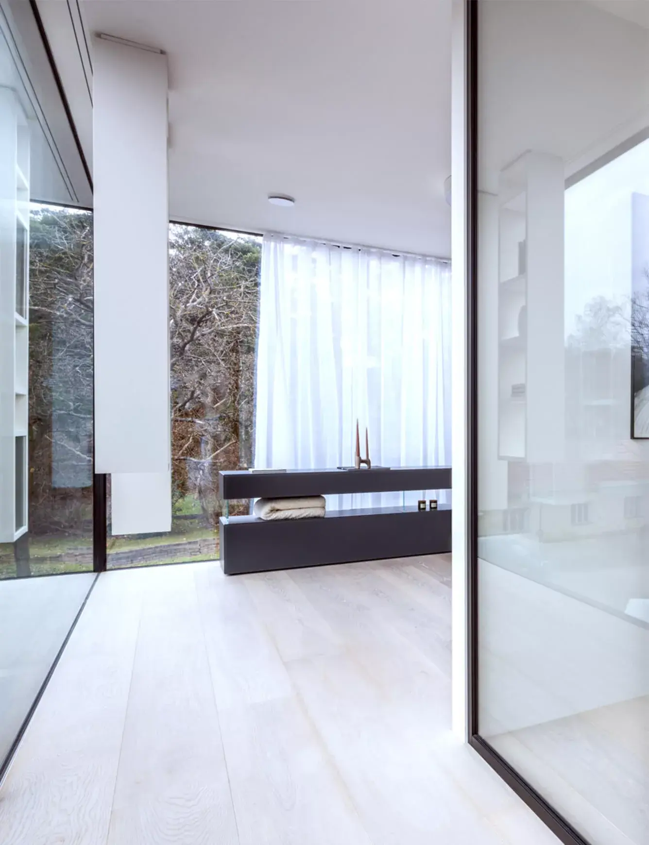 Prosluněná chodba moderní vily s velkoformátovým prosklením, kde světlá dřevěná podlaha z realizace Lago Showhouse opticky propojuje interiér s výhledem do zahrady.