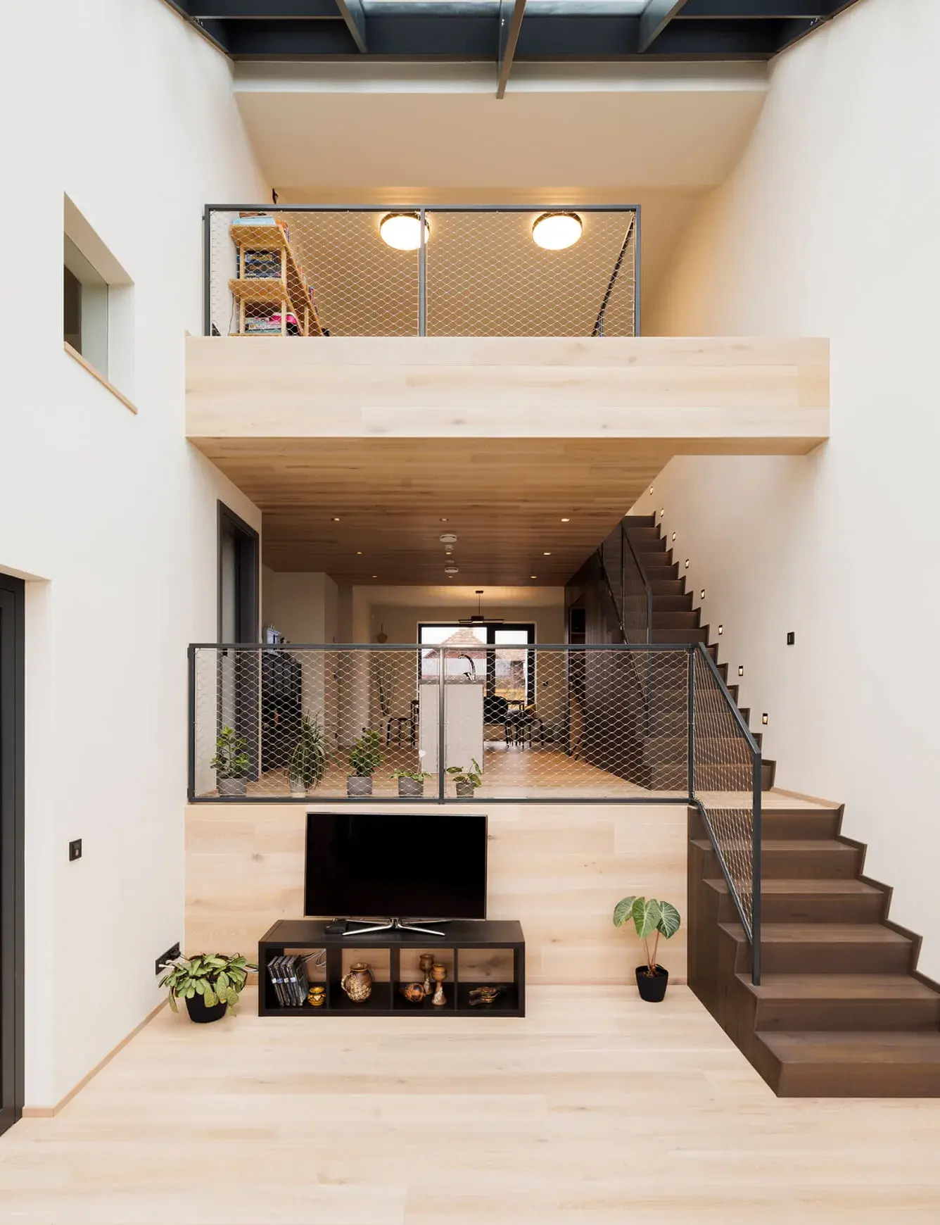 Moderní otevřený interiér rodinného domu v Židlochovicích s prosvětleným atriem, kde světlá dubová podlaha a obklady OAKCENT tvoří jemný kontrast k tmavému schodišti a industriálnímu zábradlí se sítí.