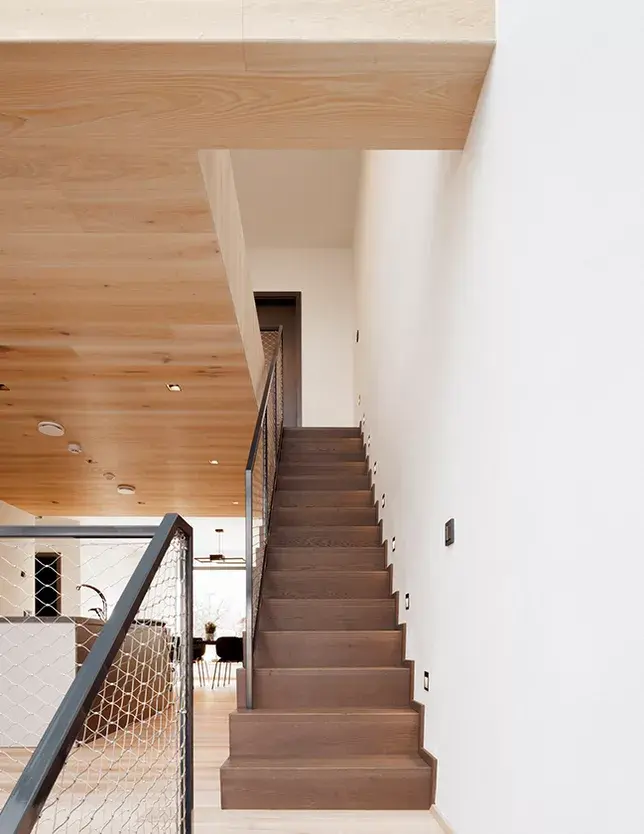 Pohled na schodiště v domě v Židlochovicích, které je precizně obloženo dubovými prkny z kolekce Hazel v kaštanově hnědé barvě, tvořící výrazný funkční kontrast k velmi světlé podlaze a stropnímu obkladu Oakcent Ivory.