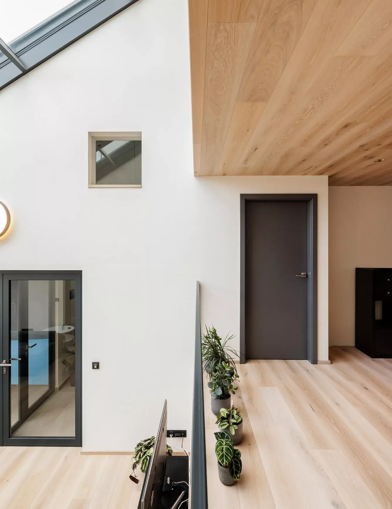 Detailní pohled na horní patro domu v Židlochovicích, kde bělená dubová podlaha a stropní obklad Oakcent Ivory kontrastují s tmavými interiérovými dveřmi a černými rámy prosklených ploch v minimalistickém bílém interiéru.