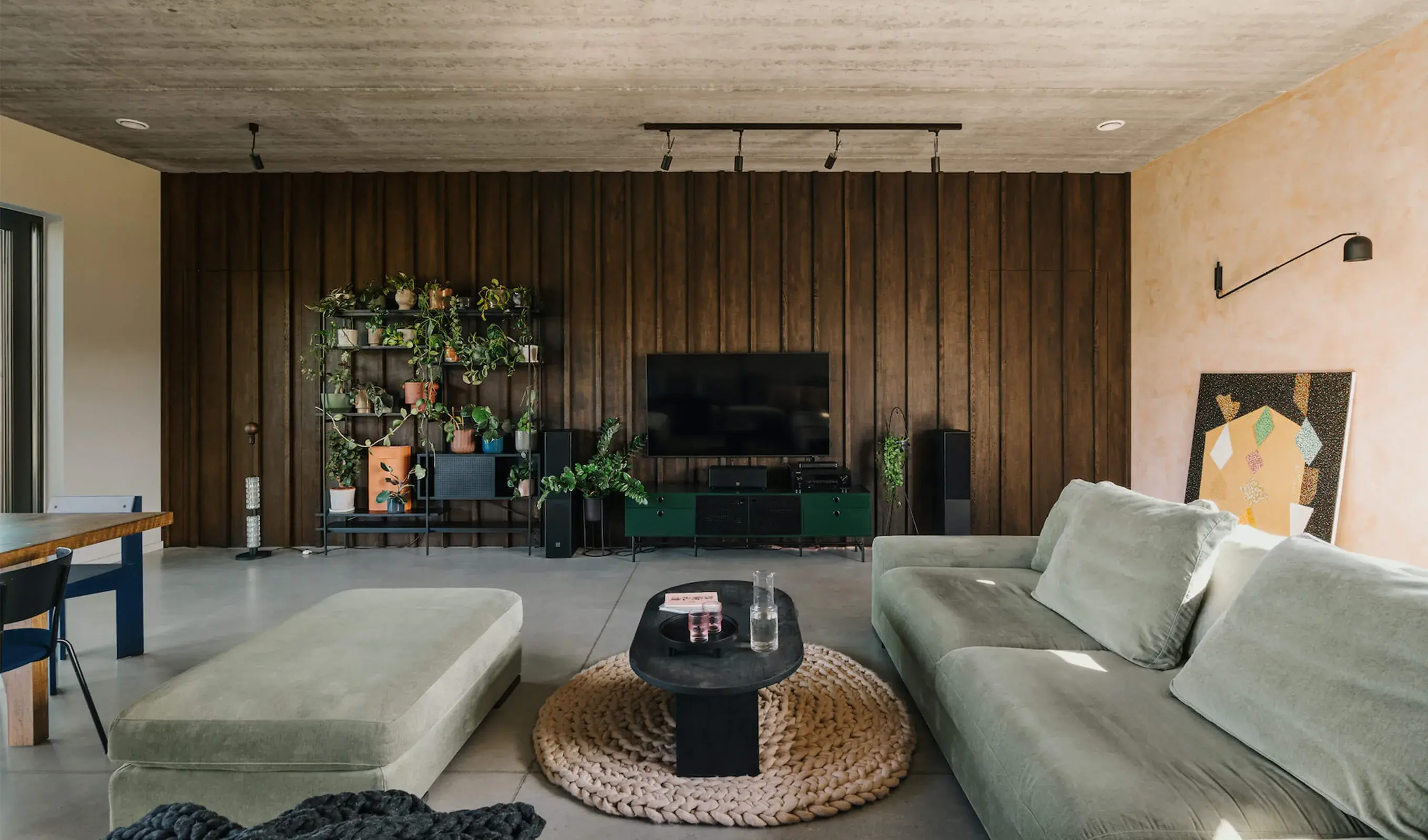 Moderní obývací pokoj v komplexně řešené stodole v Miłoslawi, kde kontrastní tmavé svislé obložení stěny doplňují podlahy z kolekce Hazel a minimalistický betonový strop s přiznaným kolejnicovým osvětlením.