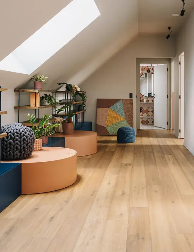 Prosvětlená chodba v podkroví stodoly v Miłoslawi, kde dubová podlaha OAKCENT harmonicky doplňuje eklektický interiér s barevnými doplňky, pokojovými rostlinami a velkým střešním oknem, které do celého prostoru přivádí přirozené denní světlo.