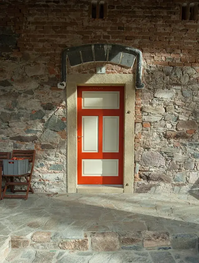 Detail vchodu do tradiční kamenné Chalupy U Cesty s výraznými červeno-bílými dřevěnými dveřmi a kamenným ostěním, doplňující rustikální eleganci exteriéru.