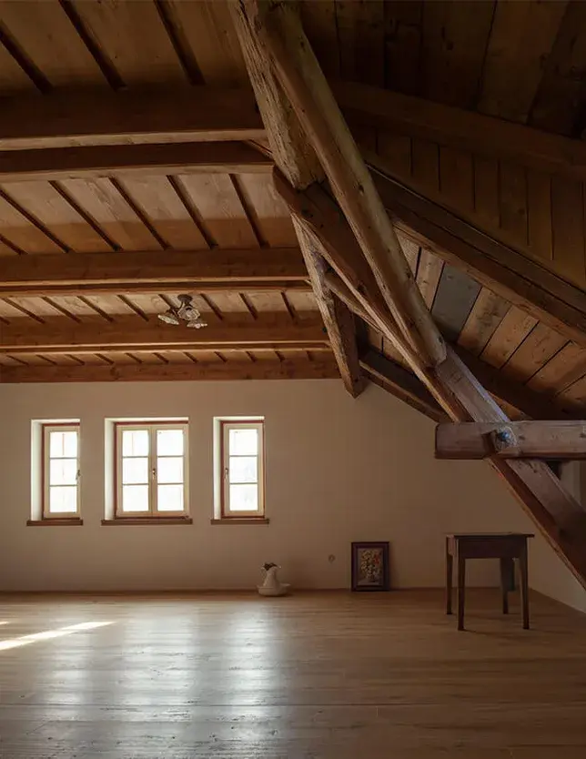 Interiér podkroví Chalupy U Cesty s odhalenou dřevěnou konstrukcí krovu, masivními trámy a třemi malými okny, které osvětlují přírodní dubovou podlahu Oakcent.