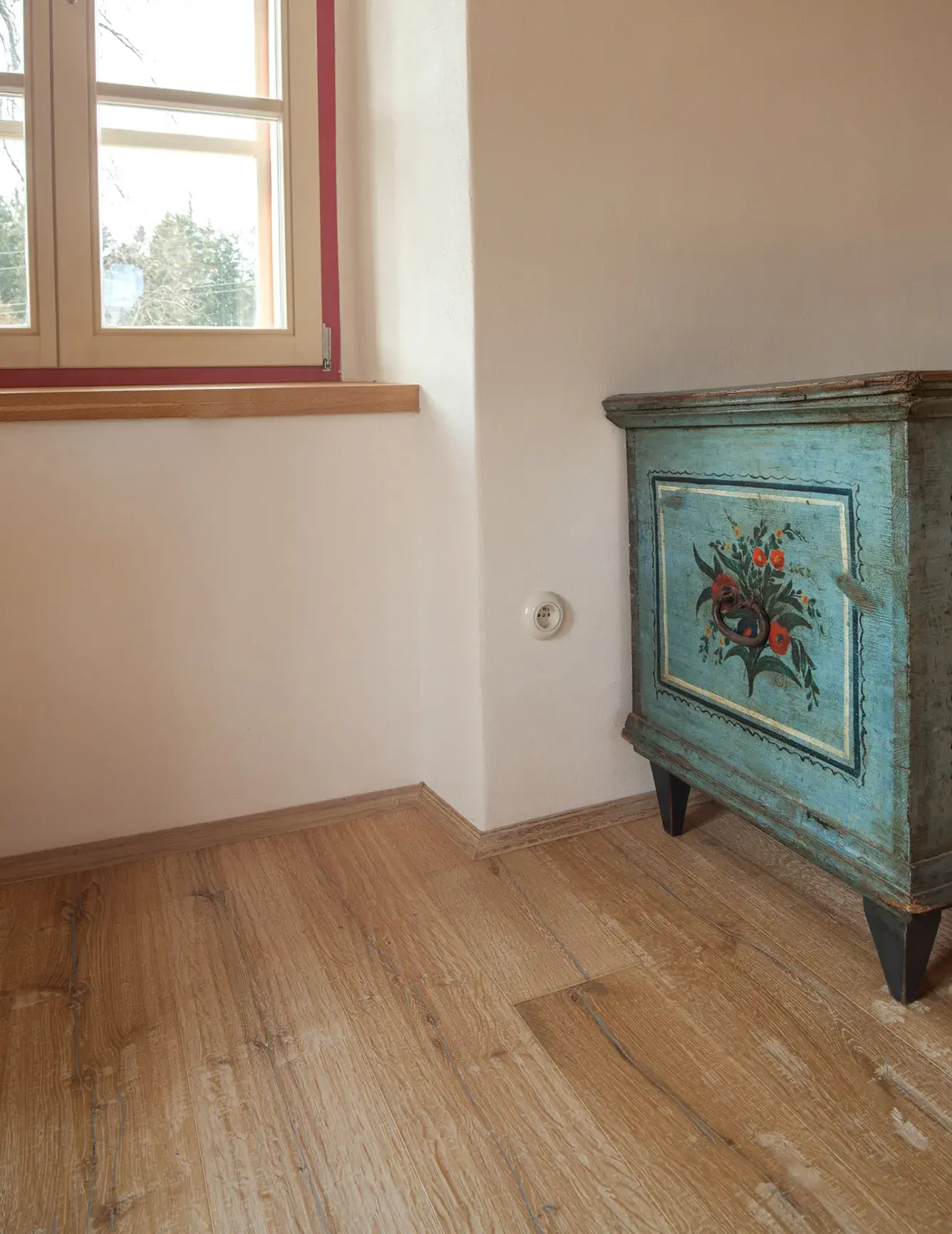 Detail interiéru Chalupy U Cesty s historickou malovanou truhlou v rohu místnosti, kde jemné přírodní světlo z okna dopadá na strukturovanou dubovou podlahu Oakcent s výraznou kresbou dřeva.