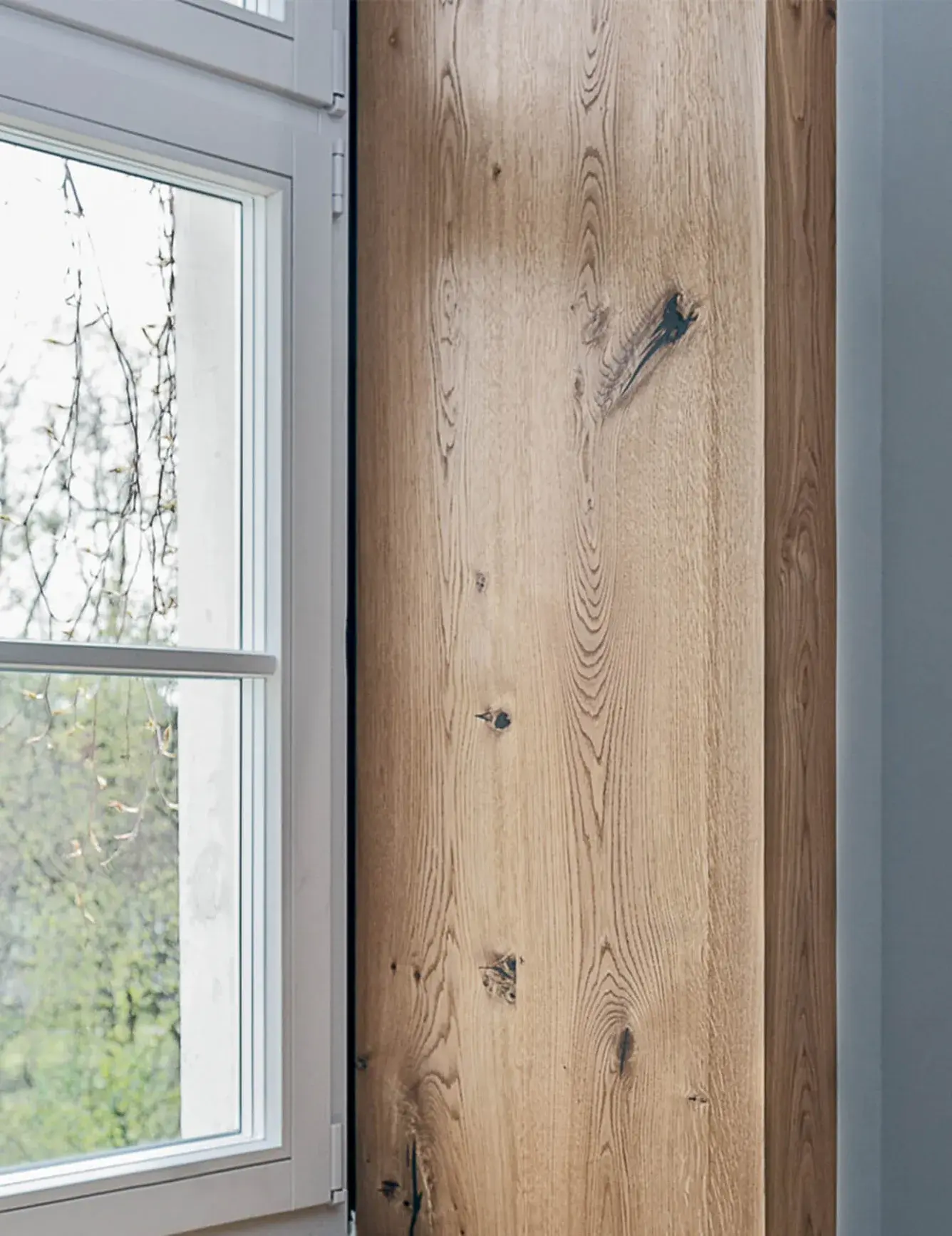 Makro detail struktury dubového dřeva použitého na hluboké okenní špaletě v apartmánu Moskal, zobrazující přirozenou kresbu letokruhů a suky v perfektním souladu s okenním rámem.