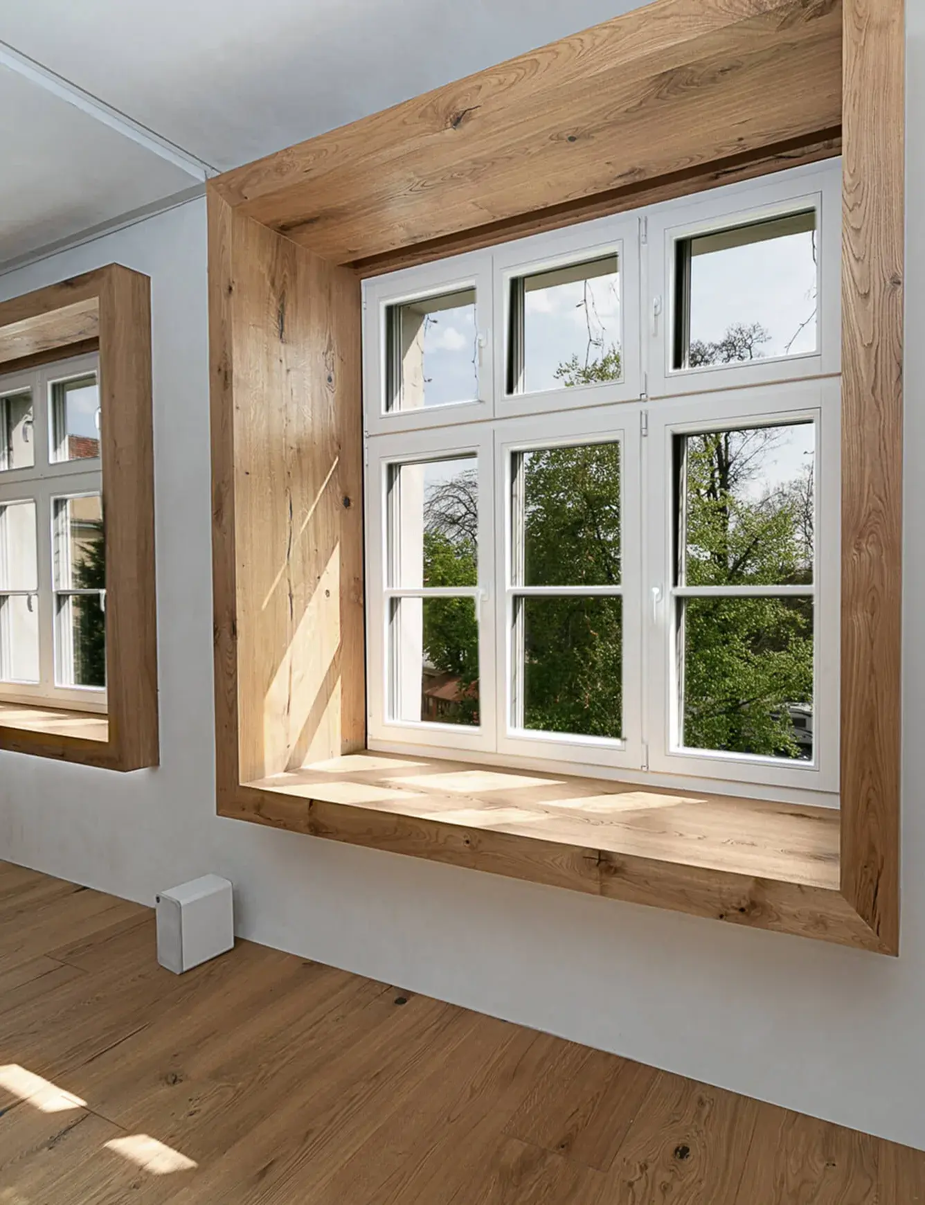 Interiér moderního soukromého apartmánu Moskal ve Vratislavi s dubovou podlahou Oakcent Rustic v přírodním olejovaném provedení, kterému dominují velká okna s hlubokým masivním dřevěným ostěním sloužícím jako parapet a výhledem do zeleně.