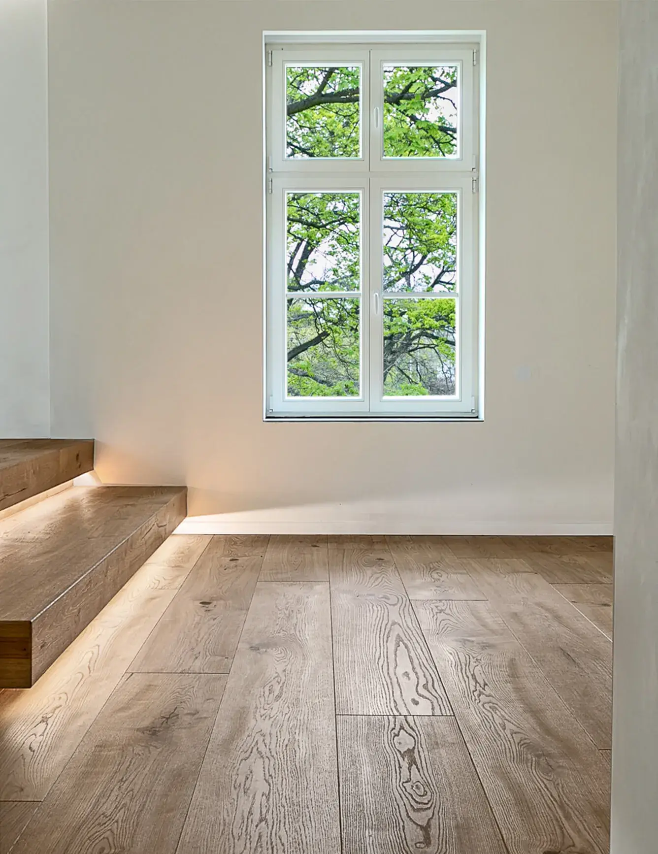 Alt: Detailní pohled na vyvýšené spací podium v apartmánu Moskal s dubovými schůdky s integrovaným LED podsvícením, které plynule navazují na podlahu Oakcent Rustic v přírodním oleji a vedou k minimalistické ložnici u okna s výhledem do zeleně.