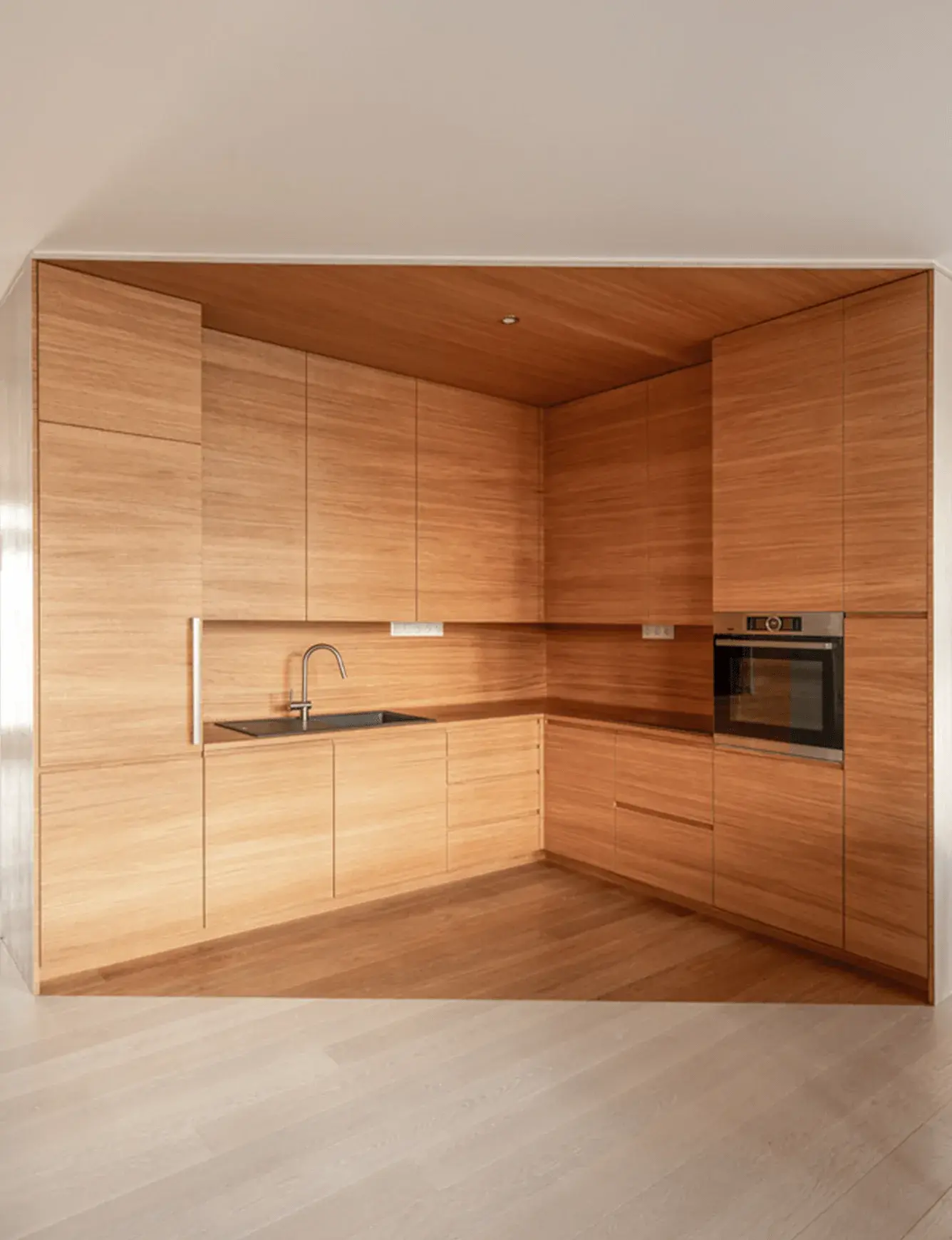 Minimalistický interiér moderní kuchyně v realizaci Káčátka s celodřevěným vestavěným nábytkem a obkladem ve světlém dubovém dekoru, který plynule navazuje na dřevěnou podlahu a vytváří kompaktní přírodní vzhled prostoru.