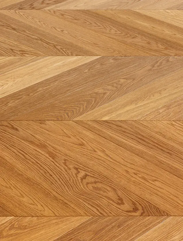 Detailní pohled na precizní kresbu dubové podlahy Oakcent Premium v provedení Chevron, která díky kartáčovanému a kouřovanému povrchu s ošetřením naturálním olejem zvýrazňuje hloubku textury a přirozenou zlatohnědou barvu dřeva v showroomu Korbička.