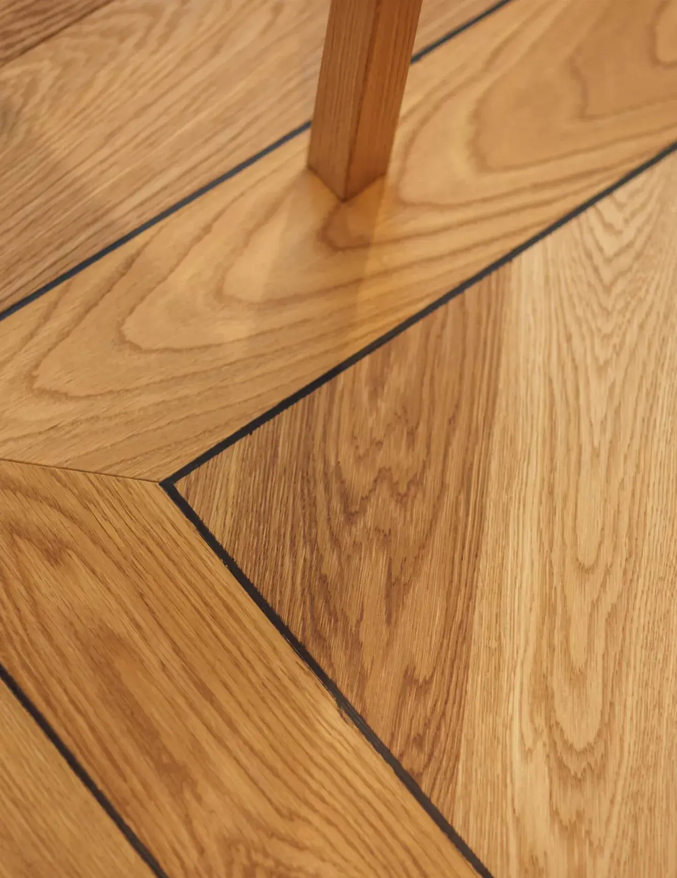 Detailní pohled na stylové zkosené napojení dubové podlahy Oakcent Premium s černou akcentovou spárou, které zdůrazňuje geometrickou přesnost vzoru Chevron v showroomu Korbička.