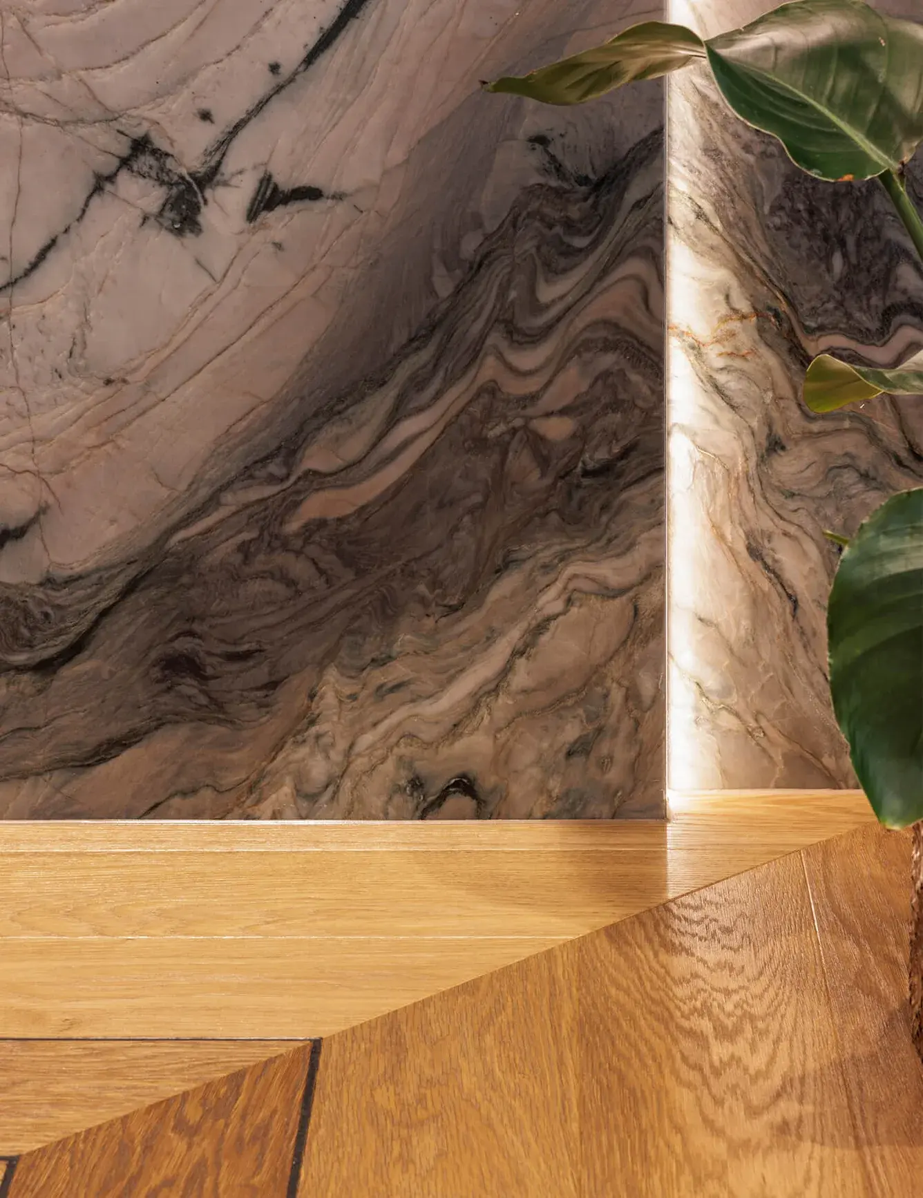 Detailní záběr na luxusní mramorovou stěnu s výraznou kresbou v showroomu Korbička, která je vertikálně podsvícená LED páskem a plynule navazuje na přírodní dubovou podlahu Oakcent Premium v precizním provedení Chevron.