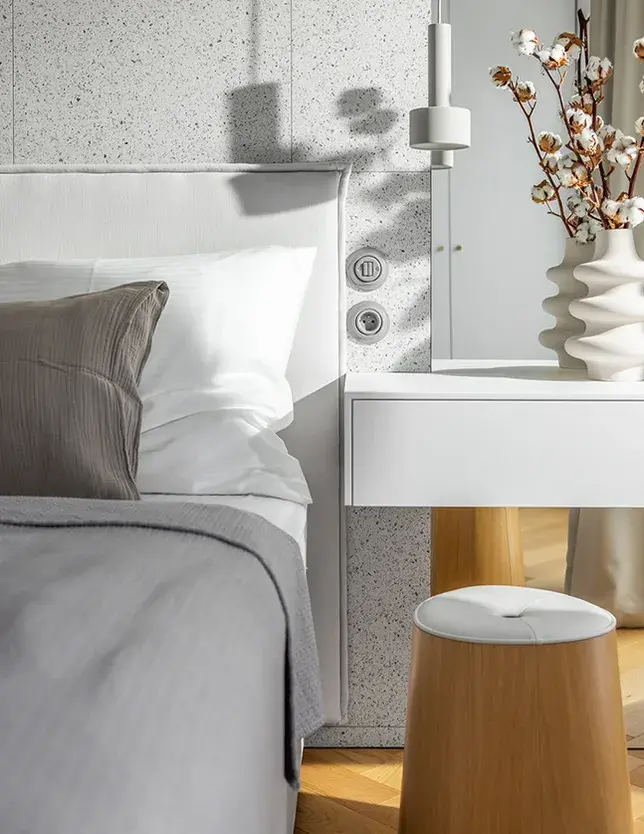 Detail ložnice v olomouckém podkrovním bytě od Cojocarů Architekti, kde se snoubí moderní prvky jako terrazzo obklad stěny a minimalistické bílé doplňky s teplým odstínem dubové podlahy Oakcent položené do vzoru rybí kosti.