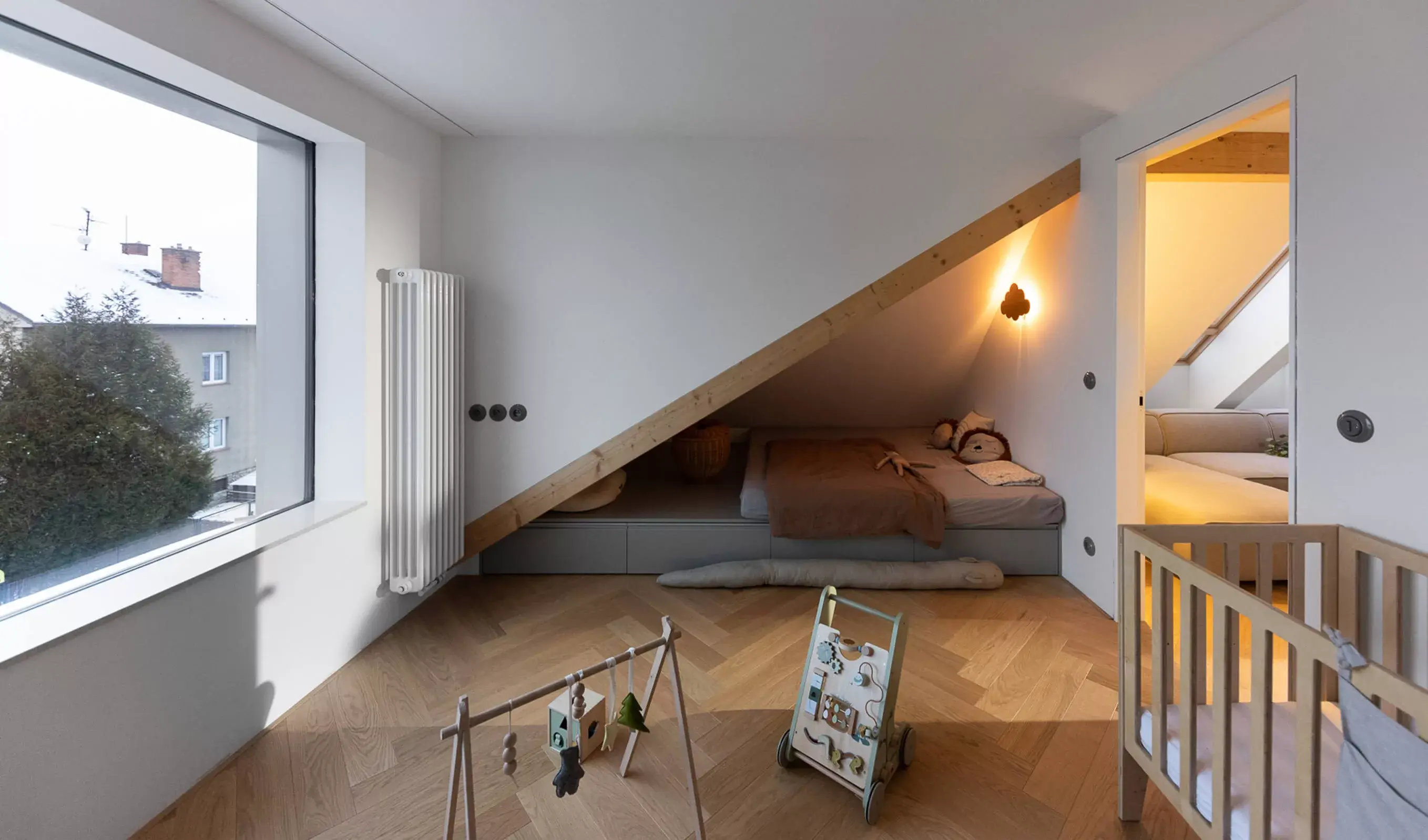 Pohled do dětského pokoje v olomouckém podkrovním bytě, kde dubová podlaha Oakcent Sand položená do vzoru rybí kosti (Herringbone) navozuje útulnou atmosféru a doplňuje minimalistické vybavení s nízkým lůžkem v šikmině pod střechou.