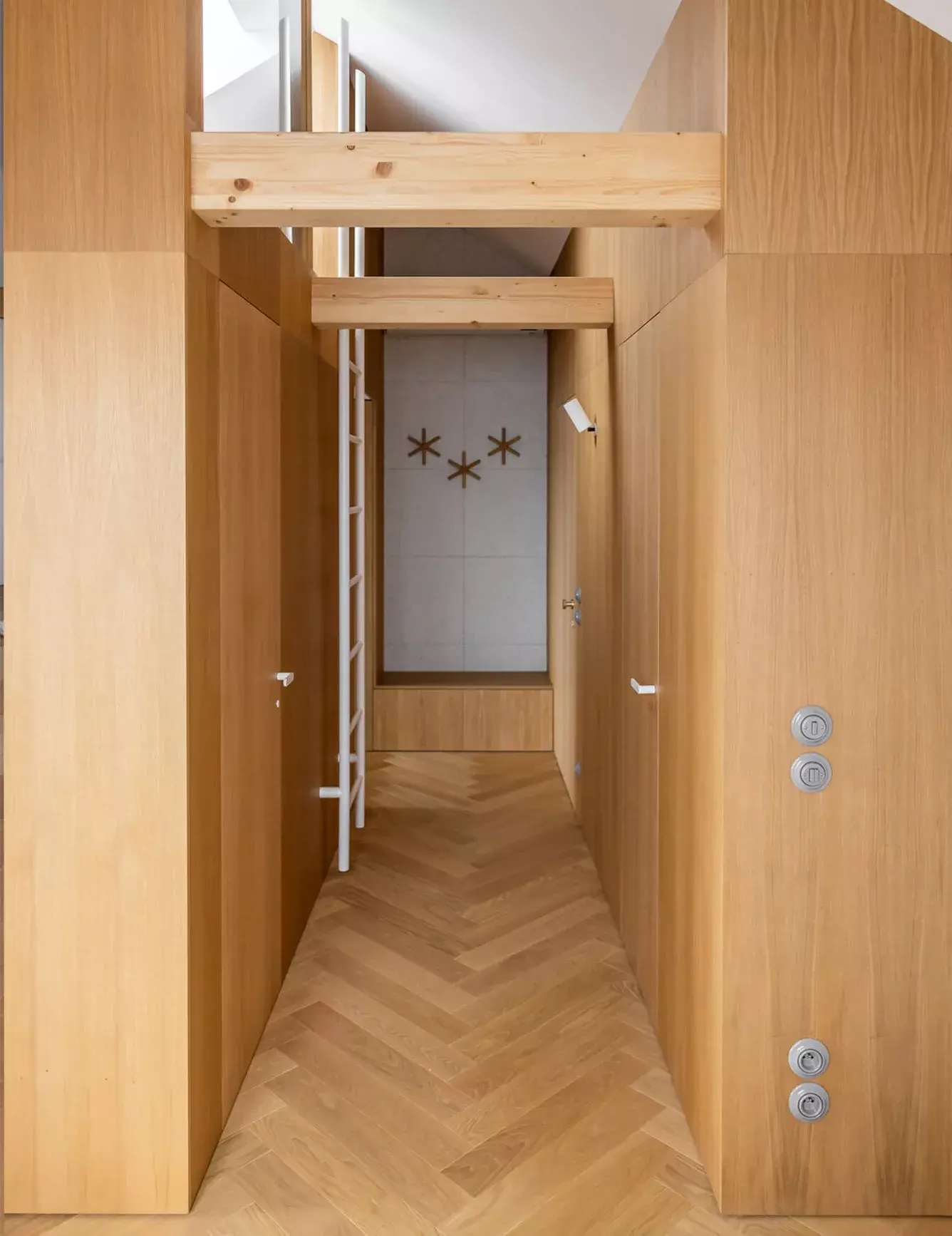 Pohled do chodby olomouckého podkrovního bytu od Cojocarů Architekti, kde se precizně zpracované dřevěné vestavby a přiznané trámy propojují s kartáčovanou dubovou podlahou Oakcent Premium položenou do vzoru rybí kosti.