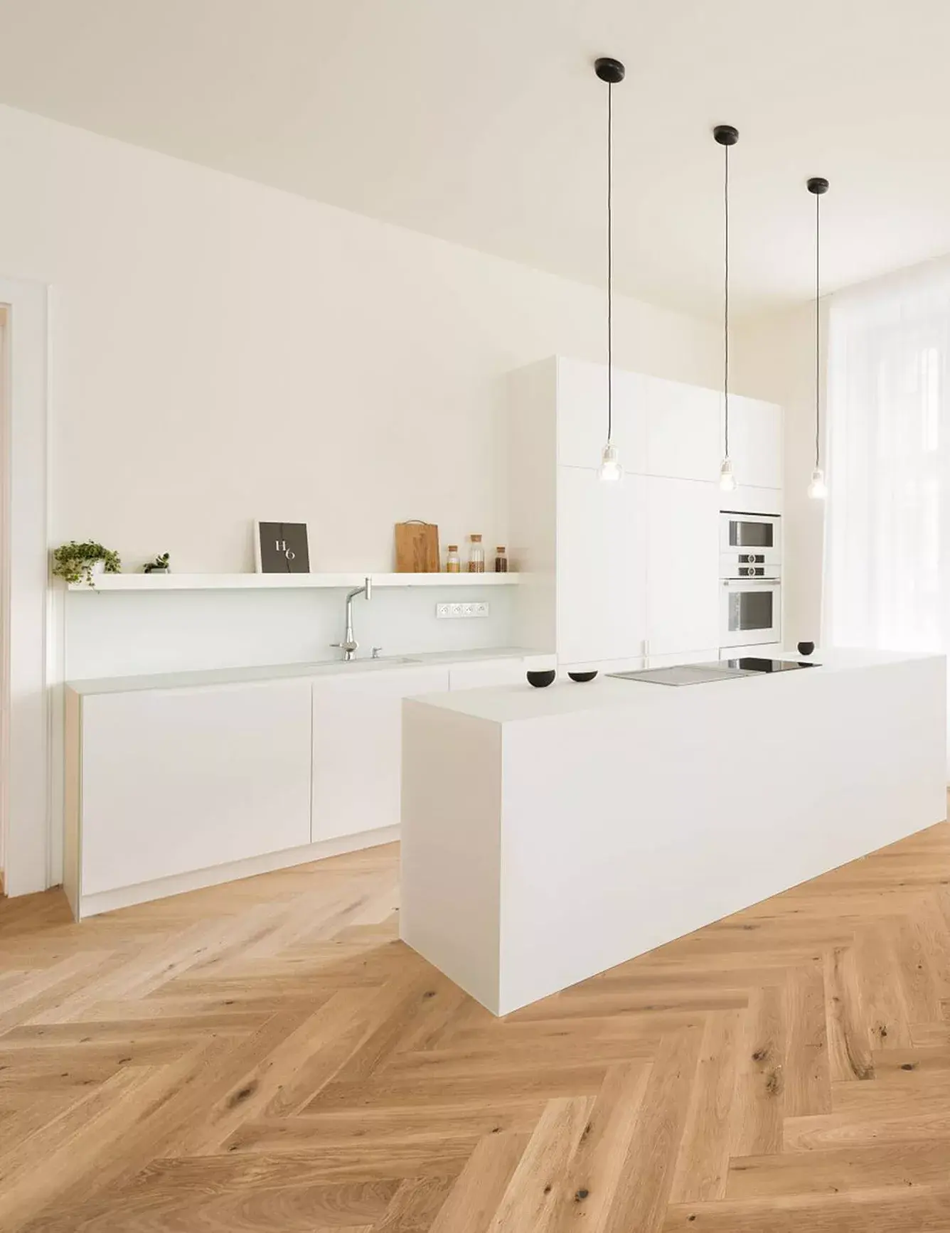 Pohled na minimalistickou bílou kuchyni s ostrůvkem v brněnském bytě, kde dubová podlaha Oakcent Rustic ve vzoru Herringbone a odstínu Light White vytváří hřejivý základ pro moderní čistý design.