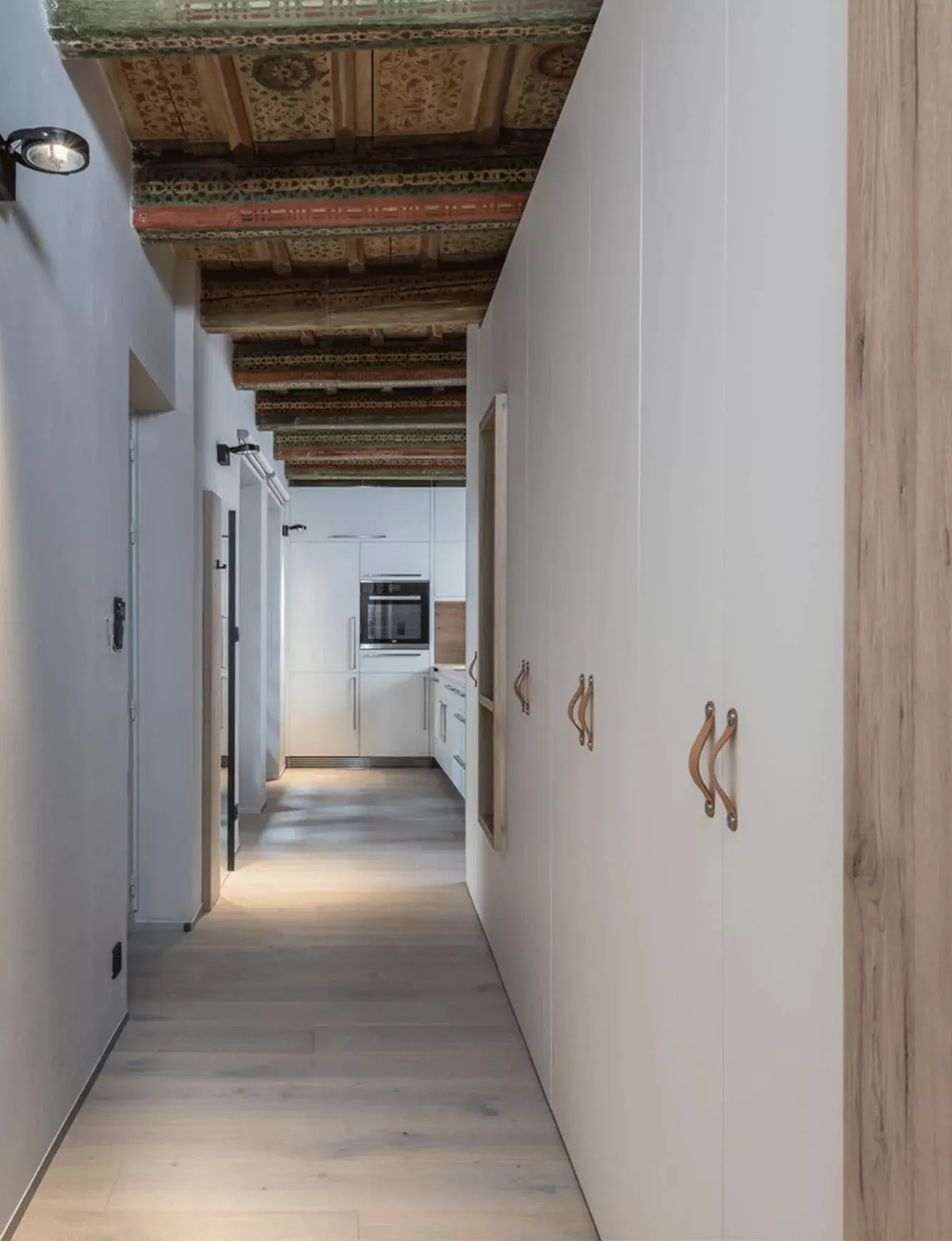 Dlouhá chodba v historickém bytě na Malé Straně s restaurovaným malovaným trámovým stropem, bílými vestavnými skříněmi s koženými úchyty a světlou dubovou podlahou Oakcent.