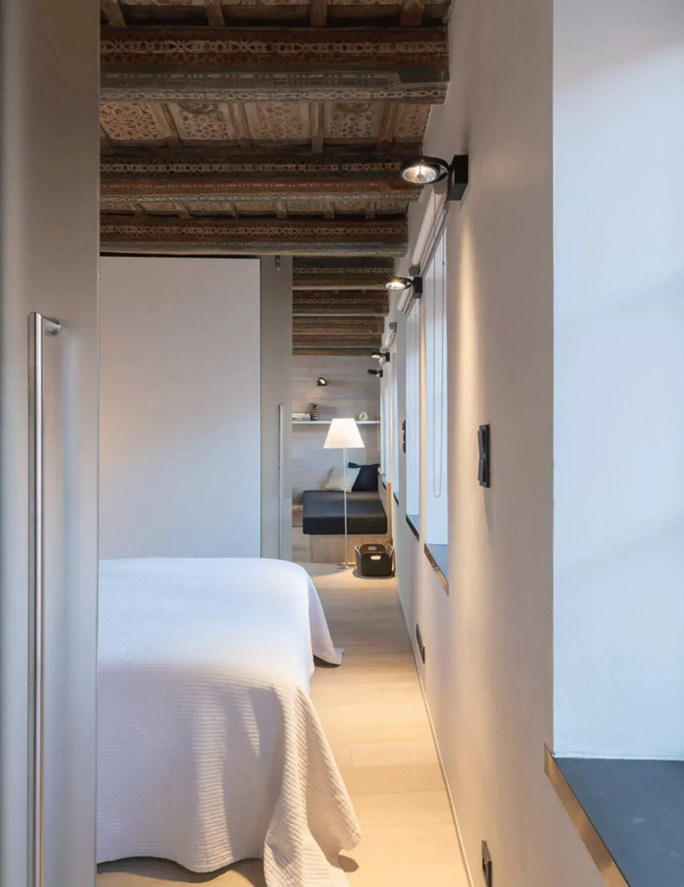 Celkový pohled na ložnicovou zónu v historickém bytě na Malé Straně, kde bílé šatní skříně a minimalistický nábytek tvoří jemný kontrast k bohatě malovanému renesančnímu stropu a světlé dubové podlaze Oakcent.